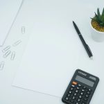 A clean workspace with a calculator, pen, paper, and a small plant.
