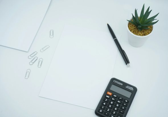 A clean workspace with a calculator, pen, paper, and a small plant.