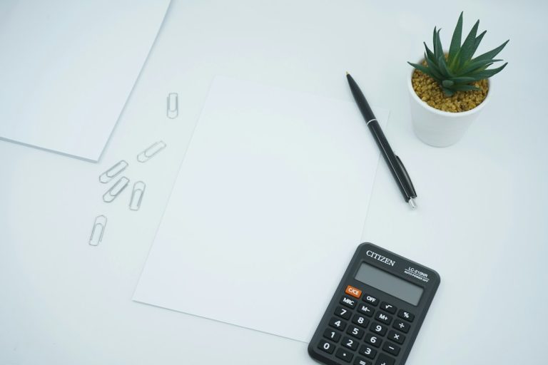A clean workspace with a calculator, pen, paper, and a small plant.
