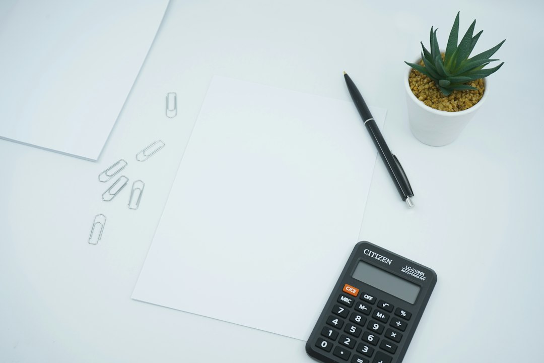 A clean workspace with a calculator, pen, paper, and a small plant.
